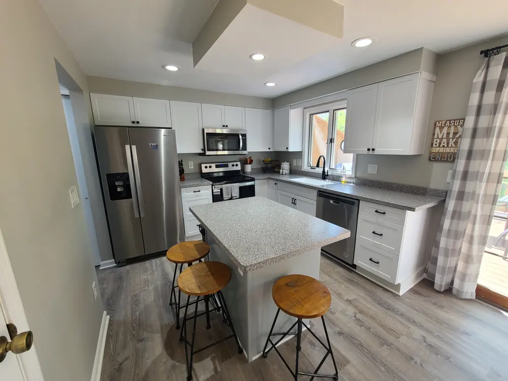 Remodeled kitchen with light cabinets, a stone-topped island and stainless steel appliances
