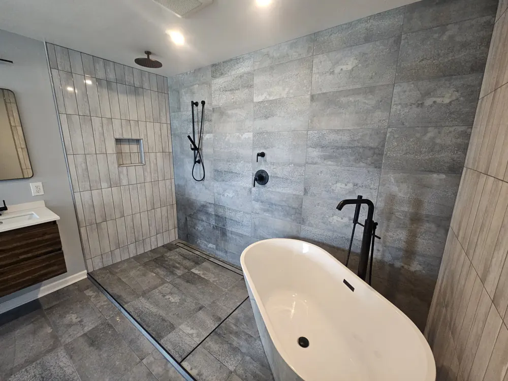 Tiled walk-in shower with black fixtures beside a freestanding soaking tub